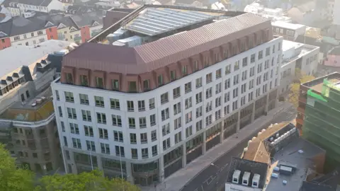 An aerial view of Jersey Government Building. It is a 7 storey building. Most of it is white other than a brown sloped roof. 