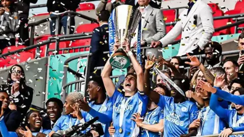 Getty Images Posh men's players, wearing their blue sports shirt, celebrating with one of them holding the golden trophy in the air and confetti in the air.