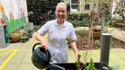 Nurse Linda Hodgkinson from the Bristol Royal Infirmary's dementia care team holds a green plastic watering can and waters chard plants at the sanctuary square garden at the Bristol Royal Infirmary