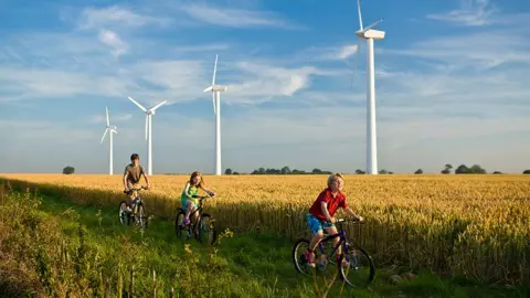 Getty Images Kids cycling past wind turbines in the country