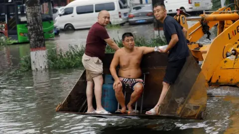 Reuters People stand on a front loader travelling through floodwaters after the rains and floods brought by remnants of Typhoon Doksuri, in Zhuozhou, Hebei province, China