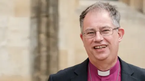 A picture of the Bishop of England, who is wearing a pink shirt and a white dog collar.