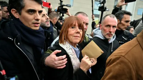 MIGUEL MEDINA/AFP Gisèle Pelicot is surrounded by family and media as she leaves court in December 2024