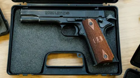 Northamptonshire Police An automatic Bruni 96 handgun which is black in colour with a brown handle. It is displayed in a box lined with foam.