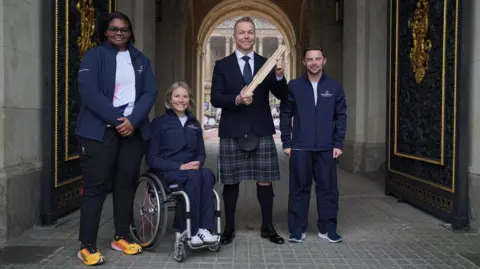 PA Sir Chris Hoy with the next three baton bearers who are wearing commonwealth games tracksuits