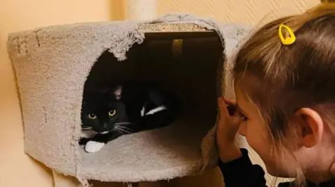 A girl looking at a black cat in a travel basket