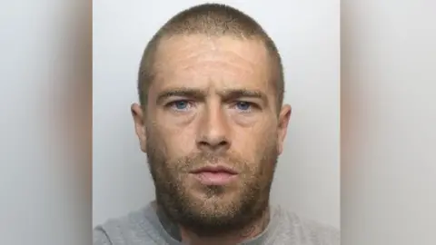 South Yorkshire Police A mugshot of Hemus who has a beard, blue eyes and a shaven head. He appears to have some tattoos around his neck area and is wearing a grey top.