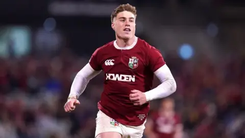 PA Media Tommy Freeman in a red British and Ireland Lions' shirt with a white undershirt and white shorts. He is running with no other players around him.