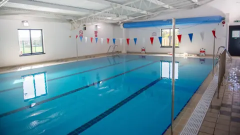Huntingdonshire District Council A photo of an indoor swimming with four lanes, taken from one side of the pool. A piece of red, white and blue bunting is dangling above it, reaching from one side of the room to the other.