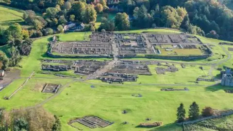 Vindolanda Trust An aerial view of Vindolanda with the Roman remains of Roman walls visible and surrounded by green fields.