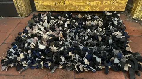 A rug on the floor near a door made up of many small rags.