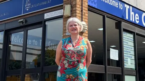 HARRIET HEYWOOD/BBC Louise Chantal is standing outside the Cresset building. It has brown bricks and electric glass doors at the entrance. She is smiling with her hands behind her back. 