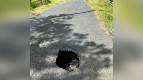 A rural road with a sinkhole about a metre wide and a couple of feet deep 