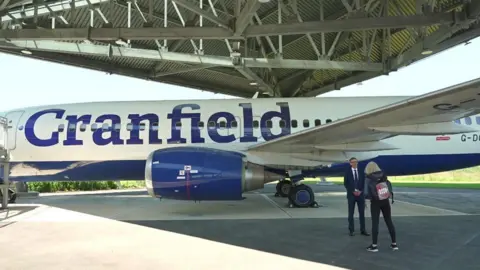 Mark Westwood being interviewed by Politics East's Amelia Reynolds beside a passenger jet 