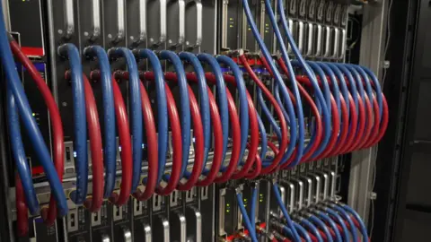 A rack of supercomputer trays, with a range of red and blue pipes plumbed into them