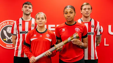 Sheffield United Four football players, two men and two women, in football kit. The women hold a gold and silver coloured baton