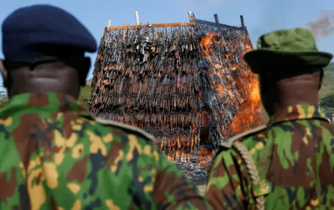 THOMAS MUKOYA / REUTERS Kenyan police officers watch as a large pyre made up of rifles and other guns is set on fire.
