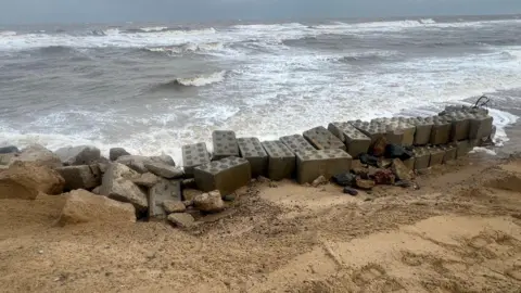 Richard Knights/BBC Dozens of large concrete blocks holding back big waves. The other side of the blocks is sand