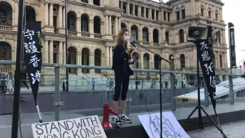 PHOEBE FAN A woman wearing a mask addresses a crowd of protesters supporting the pro-democracy demonstrators at a rally in Brisbane on 28 July