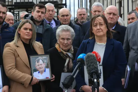 PA Media Three women stand at a microphone outside holding photos of Shawn Brown. A group of about 10 people is standing behind.