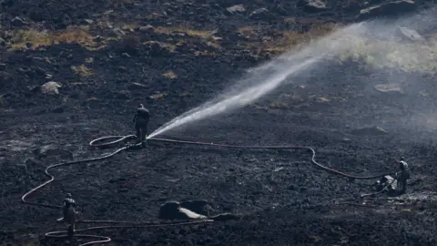 Mat Trewern/BBC Firefighter on Dove Stone spraying jets of water over the moorland.