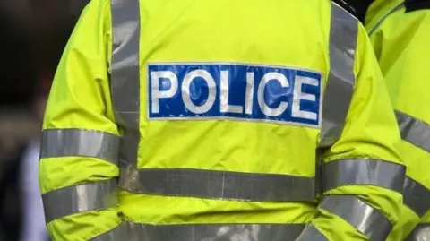 The back of a yellow high-vis police officer's coat with "POLICE" printed on the back in a blue reflective banner