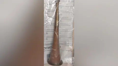 Northamptonshire Police A brass metal hunting horn inside a police evidence bag. The evidence bag has writing on it that is visible behind the horn. 