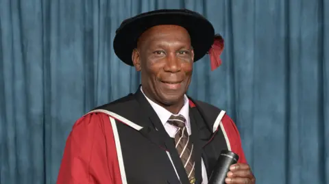 Sheffield Hallam University A man is wearing a university cap and gowns and is holding a tube with a university certificate inside