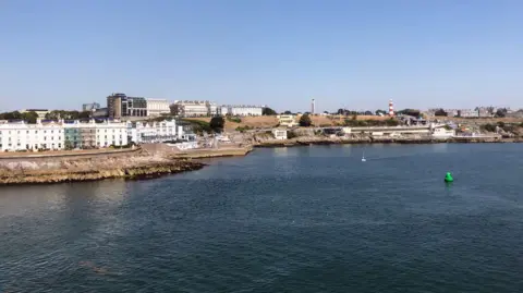 A view of Plymouth Hoe from Plymouth Sound with the red and white hoops of Smeaton's Tower seen on the right of the picture