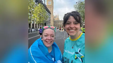 Micky Marsden Micky Marsden with brown hair tied back and green sunglasses resting on her head wearing a blue running t-shirt with the PAC charity logo and a blue flag wrapped around her stands at the finishing line of the London Marathon with her friend Lucy Reynolds. Lucy has brown hair and is wearing a turquoise, yellow and black Bowel Cancer UK running top on. They are both smiling. Big Ben and other marathon runners are seen in the background.