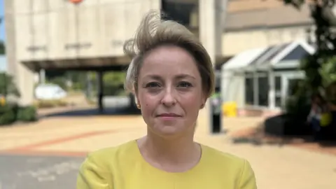 A woman in a yellow T-shirt. She has blonde hair.