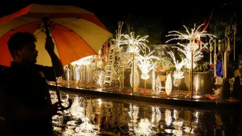 Reuters A man with an umbrella walks past decorations outside Antilia, the home of businessman Mukesh Ambani ahead of his son Anant Ambani's wedding to Radhika Merchant in Mumbai,