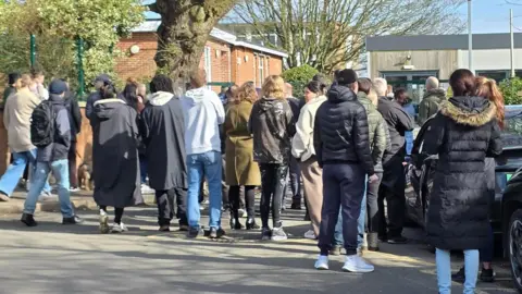 Paul Moseley/BBC A large crowd of parents waiting outside the school building.