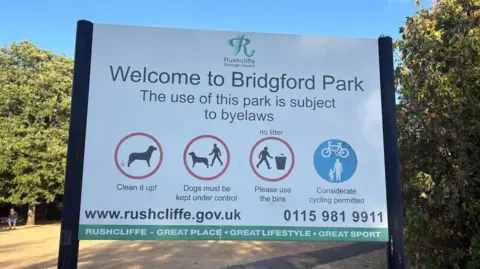 A sign welcoming people to a public park and reminding visitors of the bylaws including clearing up after dogs, not littering and riding bikes considerately.