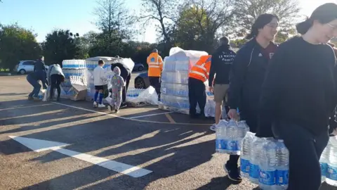 BBC Women carrying water from the bottled water supplytation