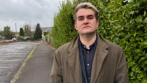 Big Brother Watch's Jake Herfert, standing between the road and the fence, looking into the camera 