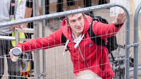 PA Media A man in a red jacket holding a cup