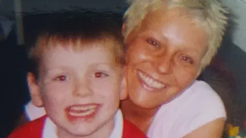 BBC Angela Frazer-Wicks pictured right, with one of her sons. They are both smiling at the camera.