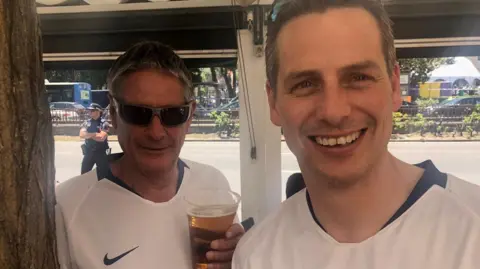 Two Tottenham fans in kit, holding pints of beer