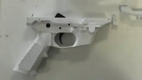 A white plastic gun made using a 3D printer on an off-white background