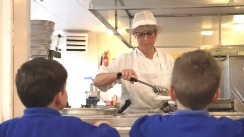 BBC Dinner lady serving two young pupils in a canteen