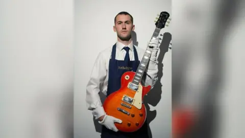 A member of staff at Sotheby's holds the guitar, which is a sunburst design.