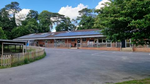 Outside image of Nettlebed Community School, which has solar panels covering its roof and is surrounded by trees and greenery