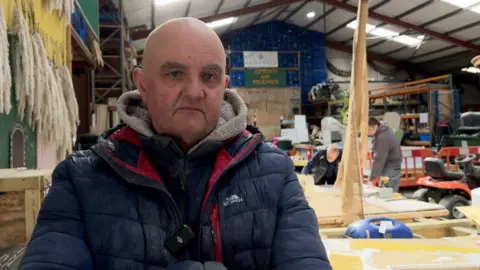 Chris Bidan wearing a jacket and looking grumpy in a workshop.