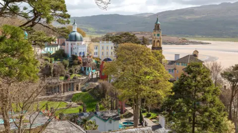 Getty Images The village has colourful buildings of different sizes, large green trees, and an estuary in the background