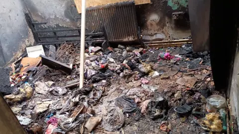 Norfolk County Council A family home after a fire with debris strewn around the floor including clothing, shoes and the springs from a burnt mattress. The walls and radiator are blackened from the flames.