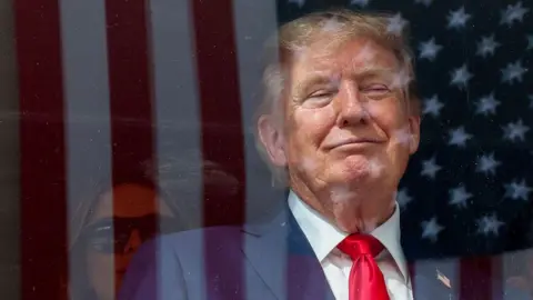 US President Donald Trump is seen behind glass which reflects the image of an American flag during an IndyCar rally in Washington DC