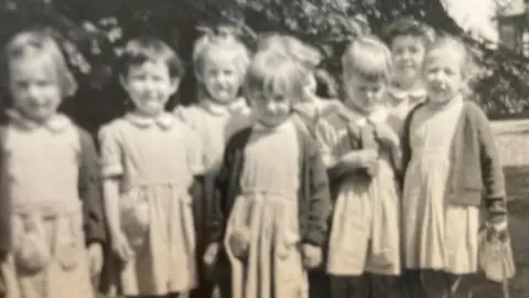 Caroline Velvick A black and white picture of young girls in school dresses.