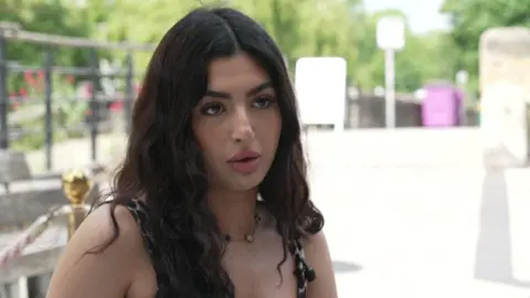 Ayla Mellek is seen sitting outdoors during a daytime interview.