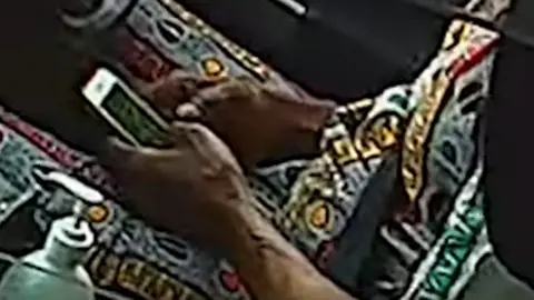 West Midlands Police Man's hand holding a mobile phone while sat in the driver's seat of a car